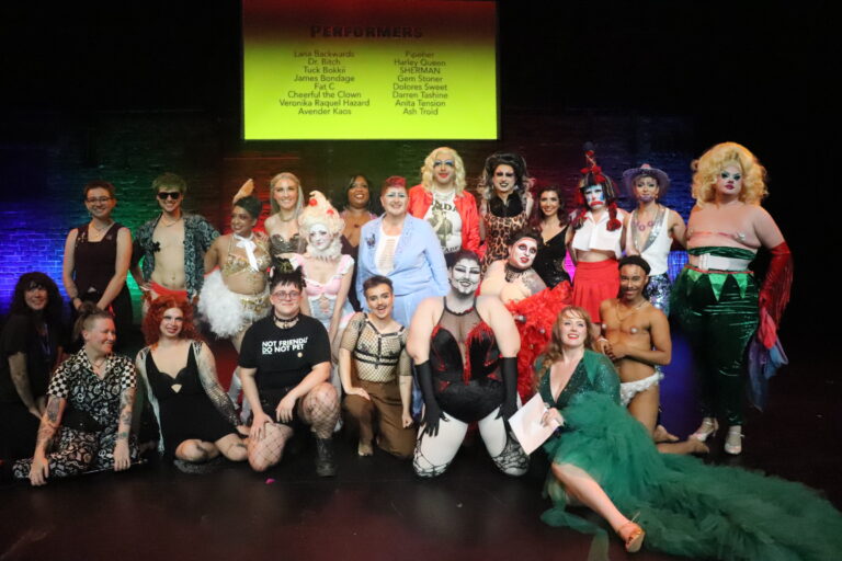 The cast and crew of the 2025 Worcester Draglesque Festival pose on stage. They are 22 drag and burlesque performers and crew in varying degrees of costume and street clothes.